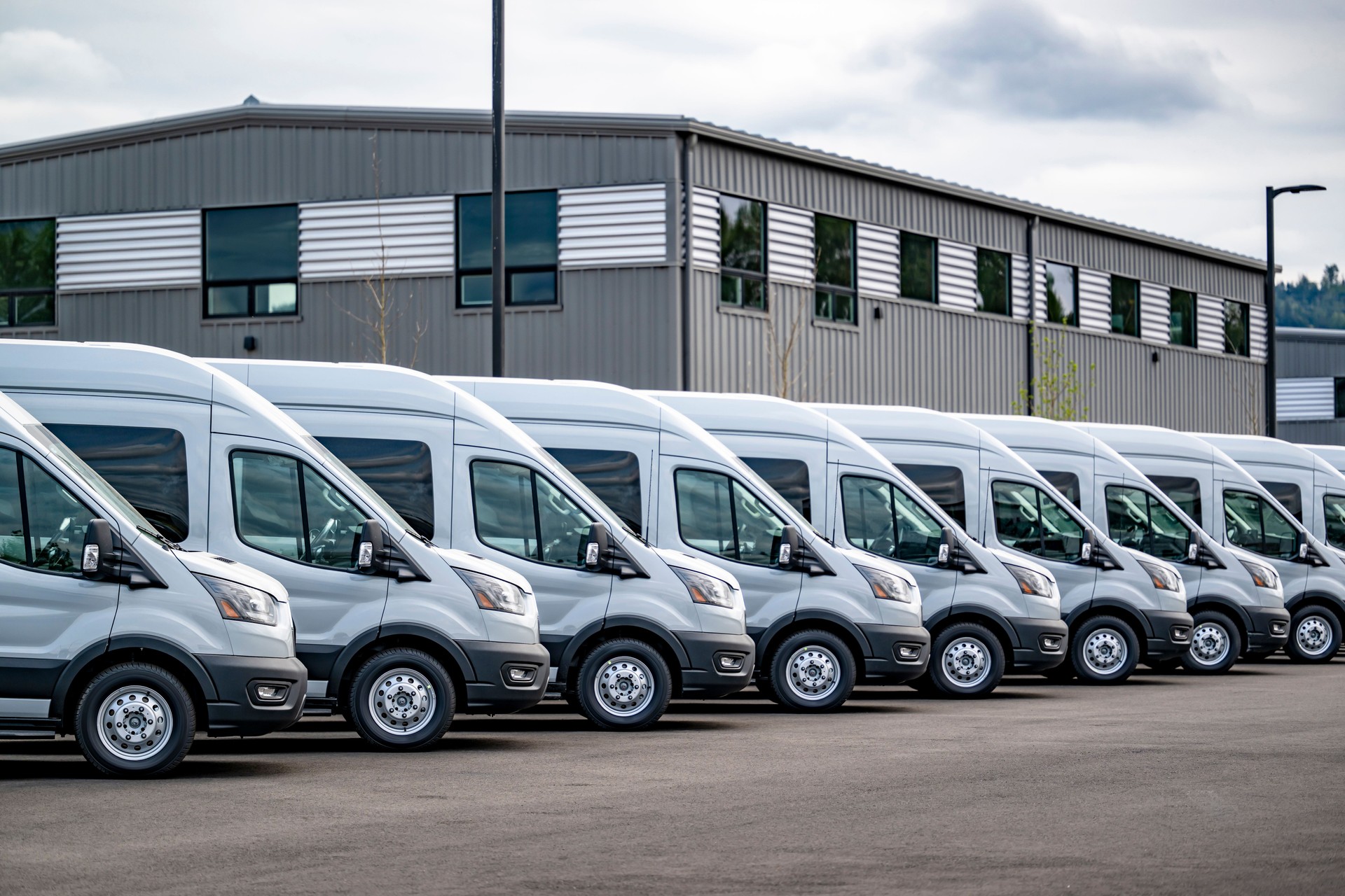 Compact gray cargo commercial mini vans standing in row on industrial warehouse parking lot waiting for the next local deliveries
